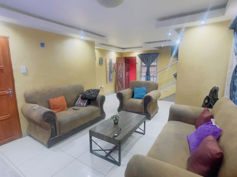 A spacious living room featuring tiled flooring, recessed ceiling lights, and an integrated staircase with a metal railing.
