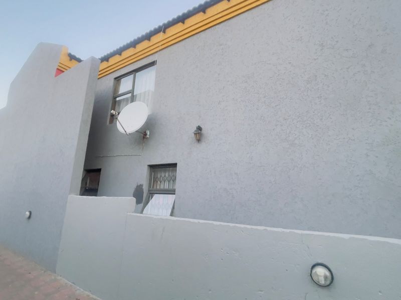 A view of the property's exterior facade featuring textured plaster walls, security gates, and mounted satellite dish.
