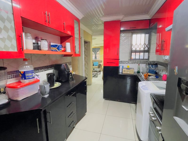 A functional kitchen featuring high-contrast red and black cabinetry, tiled flooring, and a tiled backsplash with a window security gate.