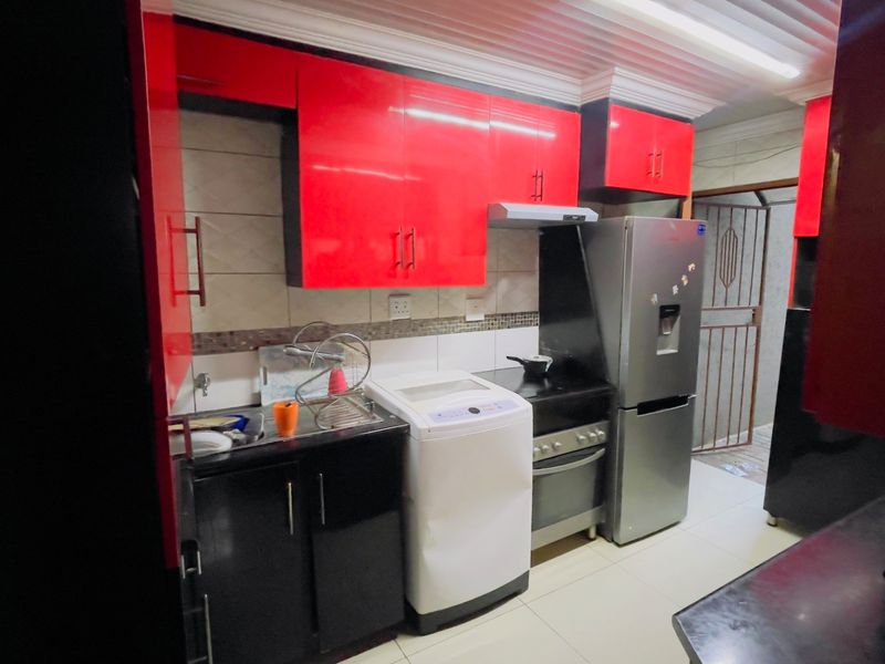 A compact kitchen featuring high-gloss red and black cabinetry, tiled backsplash, and integrated appliance space.