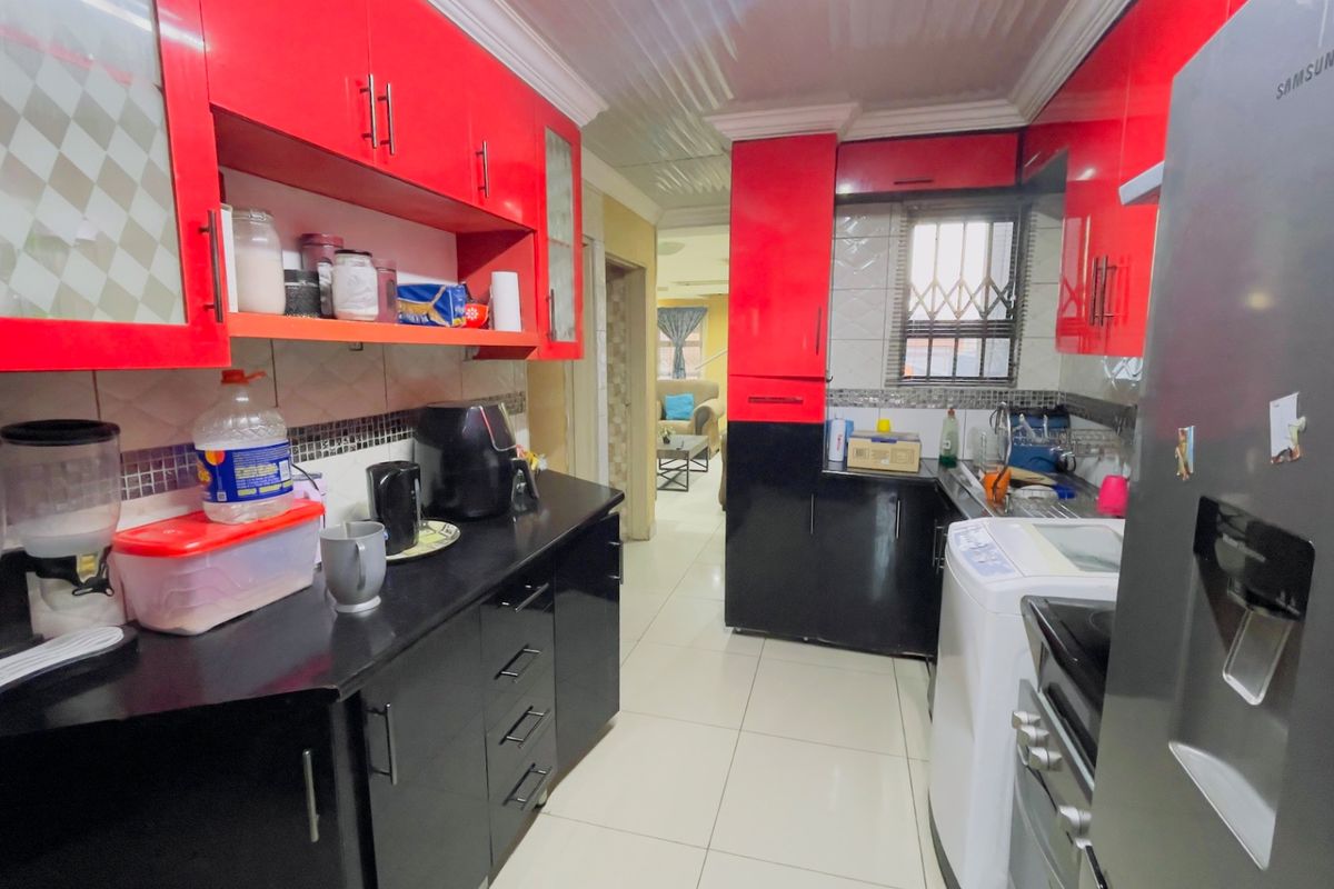 A functional kitchen featuring high-contrast red and black cabinetry, tiled flooring, and a tiled backsplash with a window security gate.