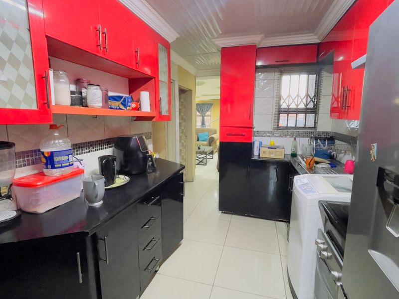 A functional kitchen featuring high-contrast red and black cabinetry, tiled flooring, and a tiled backsplash with a window security gate.