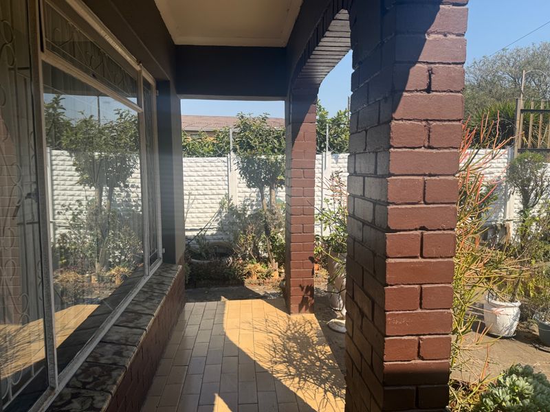 A covered patio area featuring brick pillars and tiled flooring, overlooking a private garden space with a secure boundary wall.