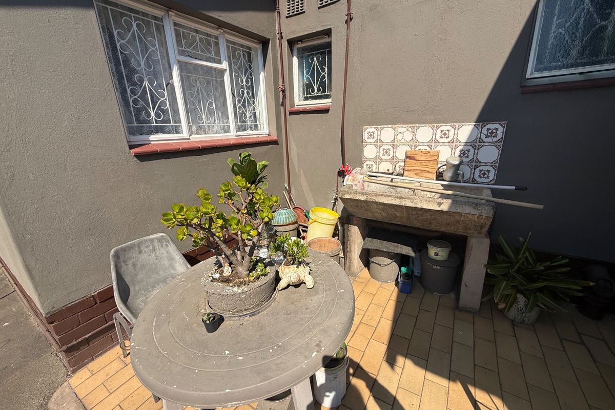 A rear exterior courtyard area featuring a traditional stone utility sink, tiled splashback, and paved flooring, suitable for outdoor utility or garden preparation.