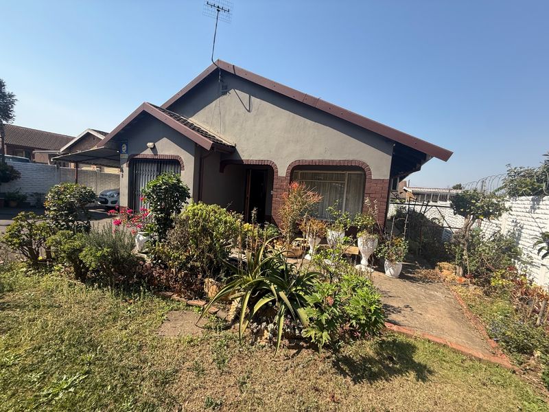 Front elevation of a single-story house featuring a tiled roof, brick accents, and a concrete driveway with established garden beds.