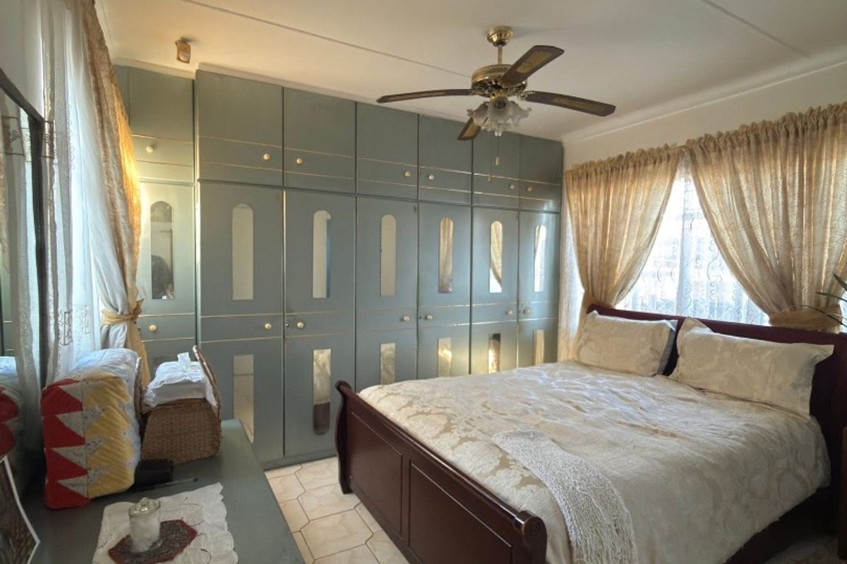 A bedroom featuring built-in cupboards with mirrored accents, a ceiling fan, and tiled flooring.