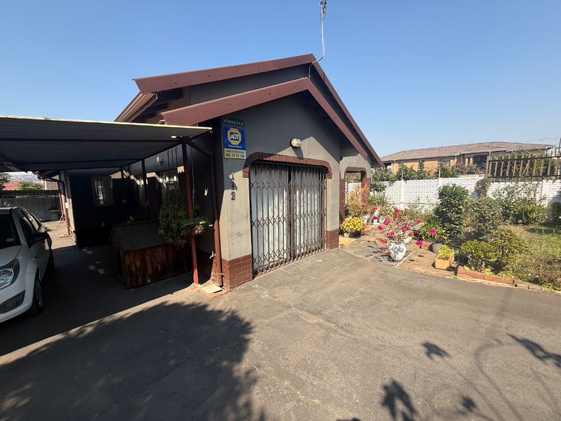 Front exterior view of the property featuring a paved driveway, attached carport, and secure gated entrance with established garden area.