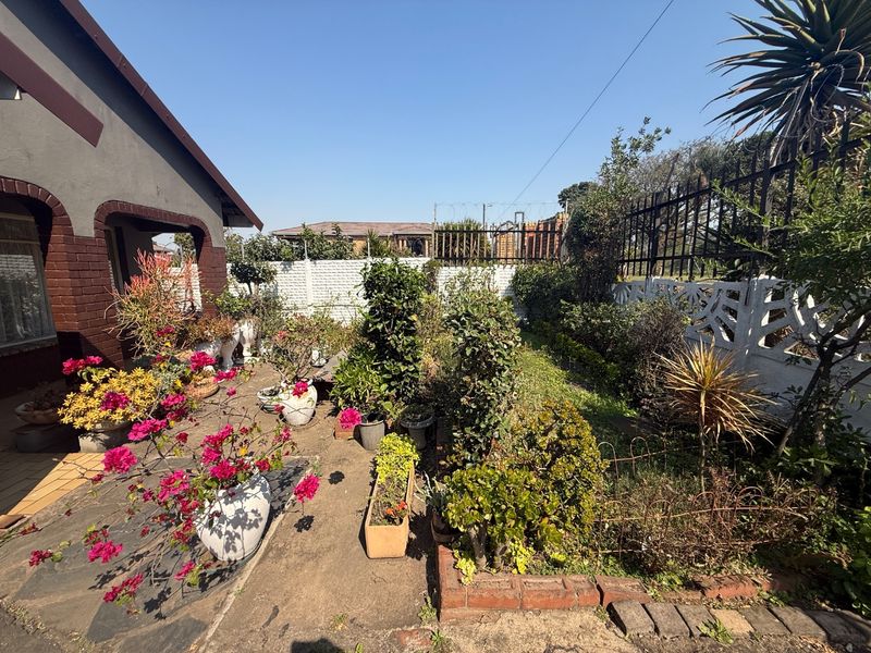 A landscaped garden area featuring a paved walkway, established shrubbery, and secure perimeter walling with metal fencing.