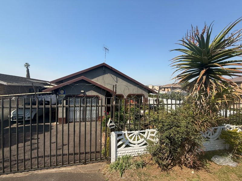 Front elevation of a residential house featuring a paved driveway, secure metal fencing with razor wire, and a concrete boundary wall.