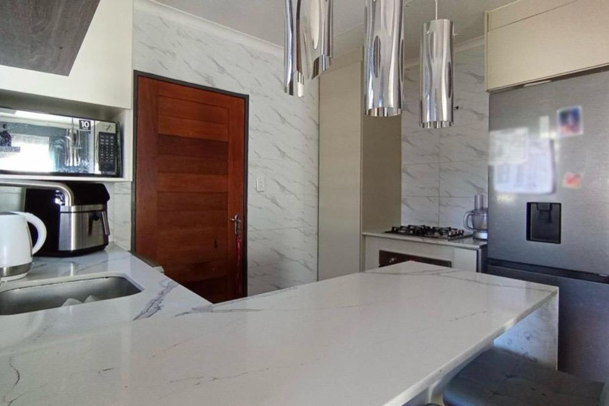 Modern kitchen featuring a marble-look quartz breakfast bar, undermount sink, built-in oven, gas hob, and contemporary pendant lighting.