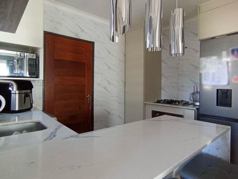 Modern kitchen featuring a marble-look quartz breakfast bar, undermount sink, built-in oven, gas hob, and contemporary pendant lighting.