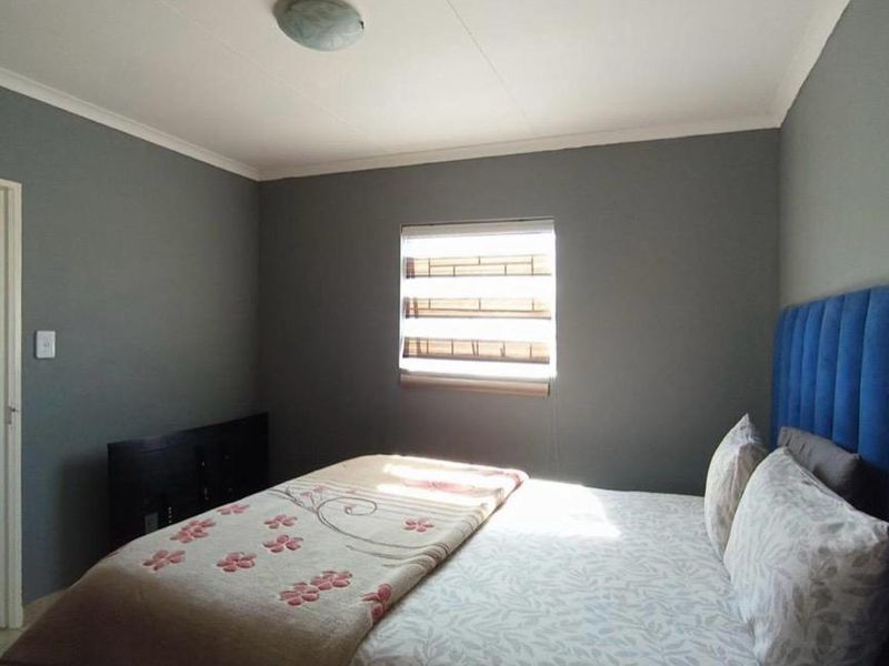 A well-maintained bedroom featuring grey painted walls, a window with security bars, and a coved ceiling.