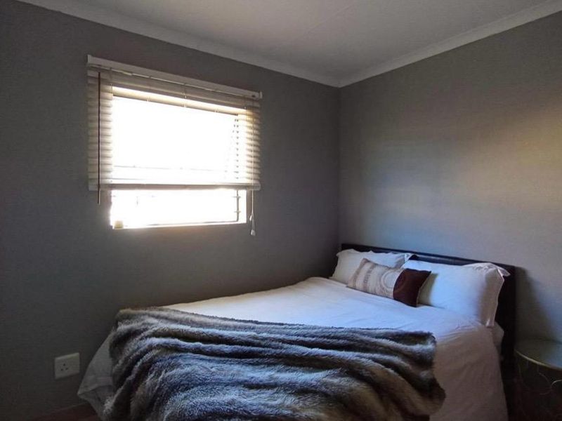 A neutrally painted bedroom featuring a window with fitted venetian blinds and decorative ceiling coving.