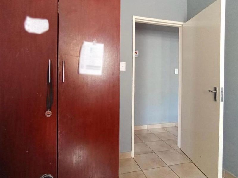 A bedroom featuring a built-in wooden wardrobe and tiled flooring, leading into an adjacent hallway area.