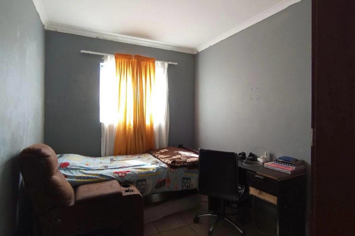 A compact bedroom featuring tiled flooring and coved ceilings, currently utilized as a combined sleeping and study area.