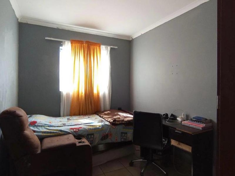 A compact bedroom featuring tiled flooring and coved ceilings, currently utilized as a combined sleeping and study area.