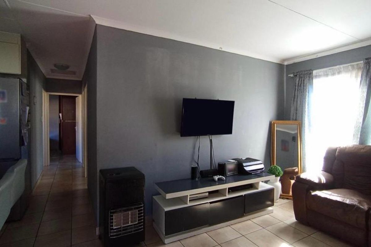 A living room featuring tiled flooring, a wall-mounted gas heater, and neutral grey wall finishes, providing a functional and comfortable living space.
