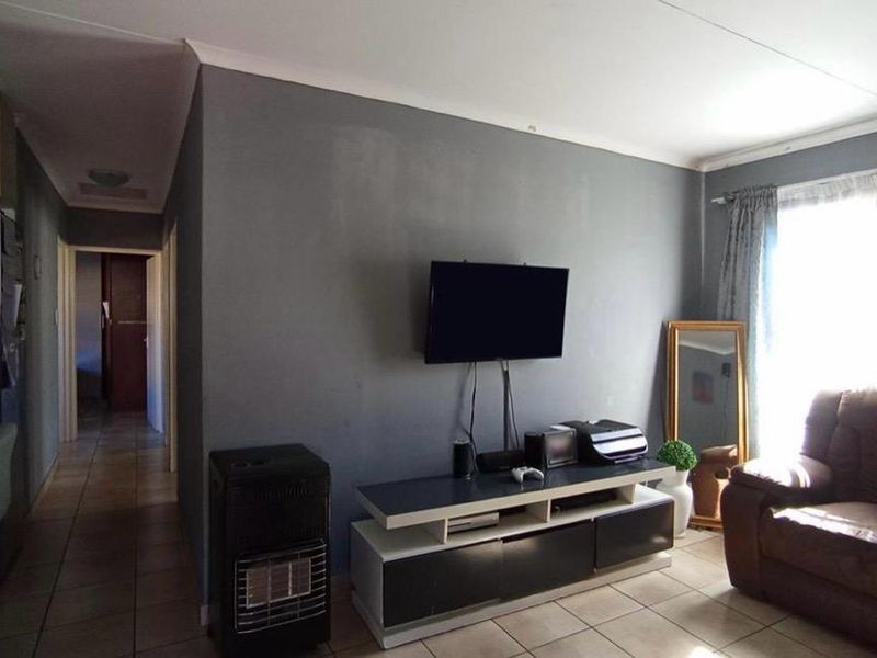 A living room featuring tiled flooring, a wall-mounted gas heater, and neutral grey wall finishes, providing a functional and comfortable living space.