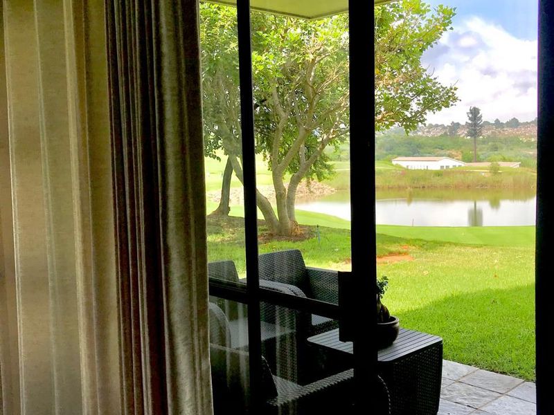 A covered patio featuring slate tile flooring and a sliding glass door, offering a scenic view of the garden and lake.