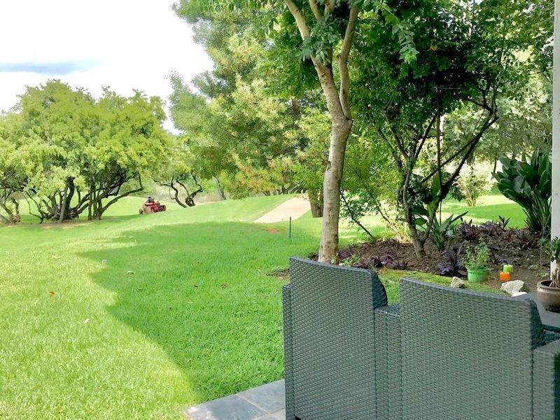 A covered patio featuring slate tile flooring, overlooking a lush green garden and landscaped lawn area.