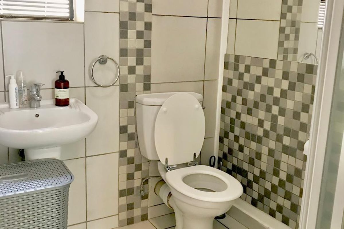 A functional bathroom featuring a pedestal basin, toilet, and a shower enclosure with decorative mosaic tile accents and tiled flooring.
