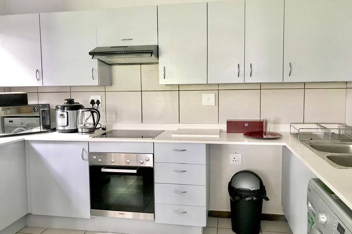 A functional kitchen featuring light-toned cabinetry, a built-in oven with electric hob, extractor fan, tiled backsplash, and a double sink.