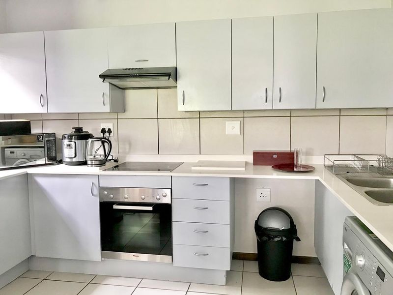 A functional kitchen featuring light-toned cabinetry, a built-in oven with electric hob, extractor fan, tiled backsplash, and a double sink.