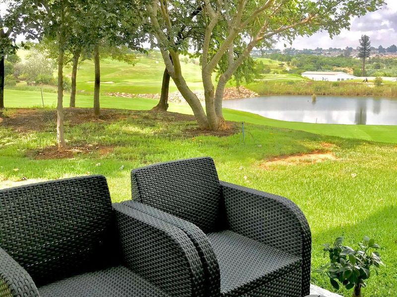 A scenic outdoor view overlooking a lush green golf course, manicured garden, and a tranquil lake.