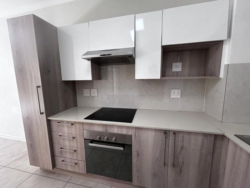 Modern kitchen featuring sleek two-tone cabinetry, stone countertops, integrated electric hob, oven, and extractor fan with a clean tiled backsplash.
