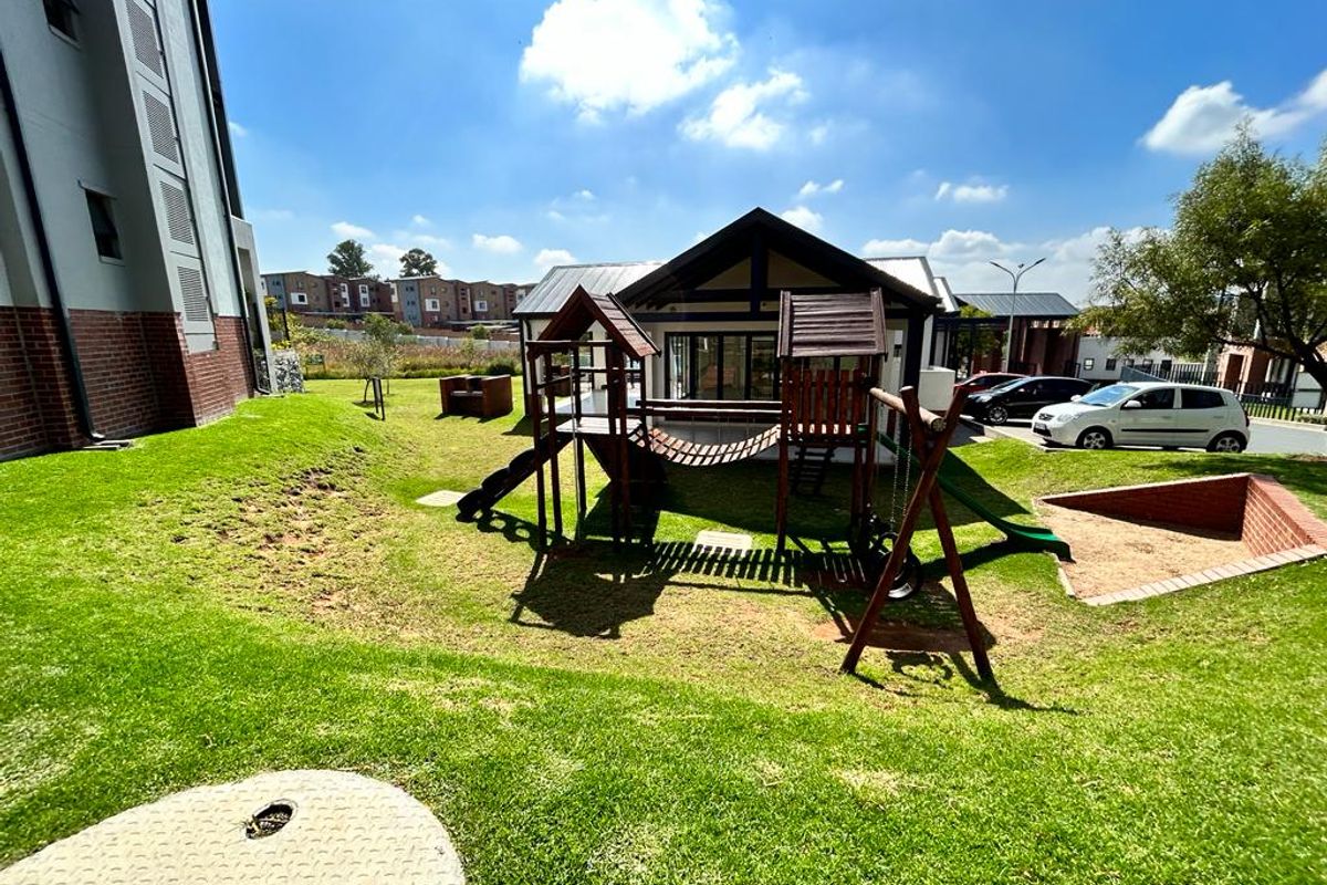 A well-maintained communal garden area featuring a lawn, brick retaining wall, and playground equipment within an apartment complex setting.