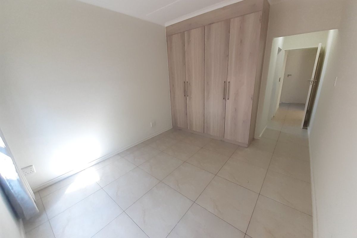 A bright, empty bedroom featuring neutral tiled flooring and modern built-in wooden cupboards, offering a clean and versatile space.
