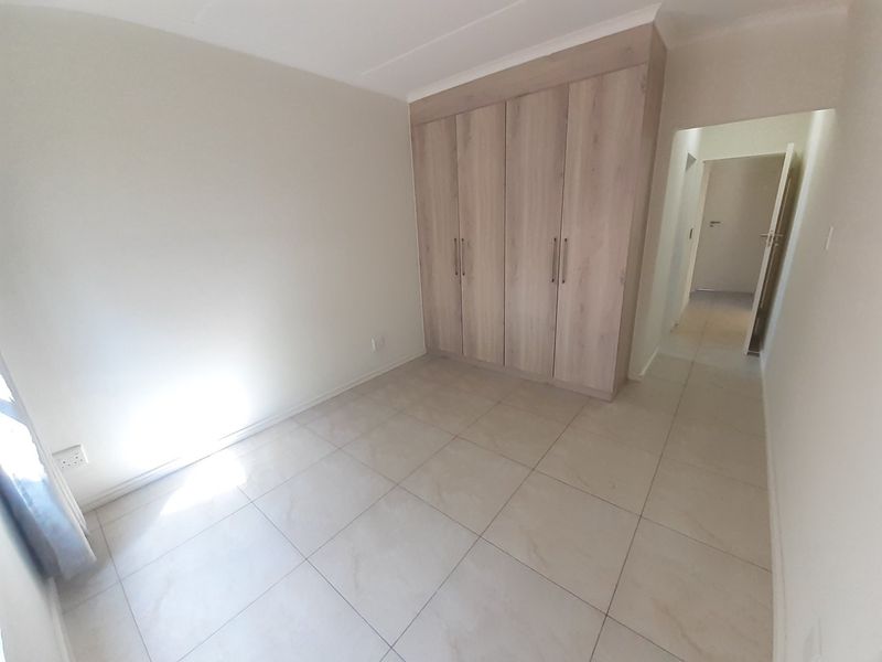 A bright, empty bedroom featuring neutral tiled flooring and modern built-in wooden cupboards, offering a clean and versatile space.