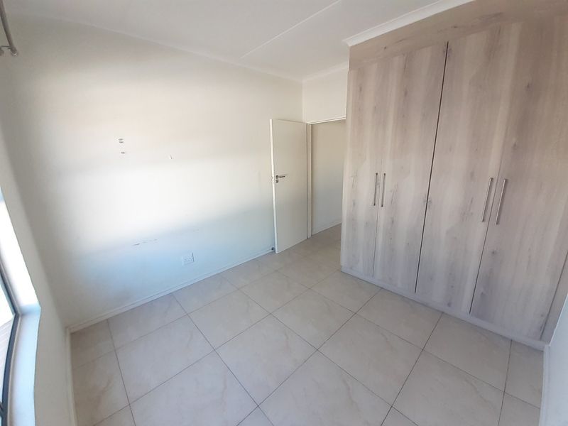 An empty bedroom featuring light-toned built-in cupboards, neutral tiled flooring, and clean white walls, ready for personalization.