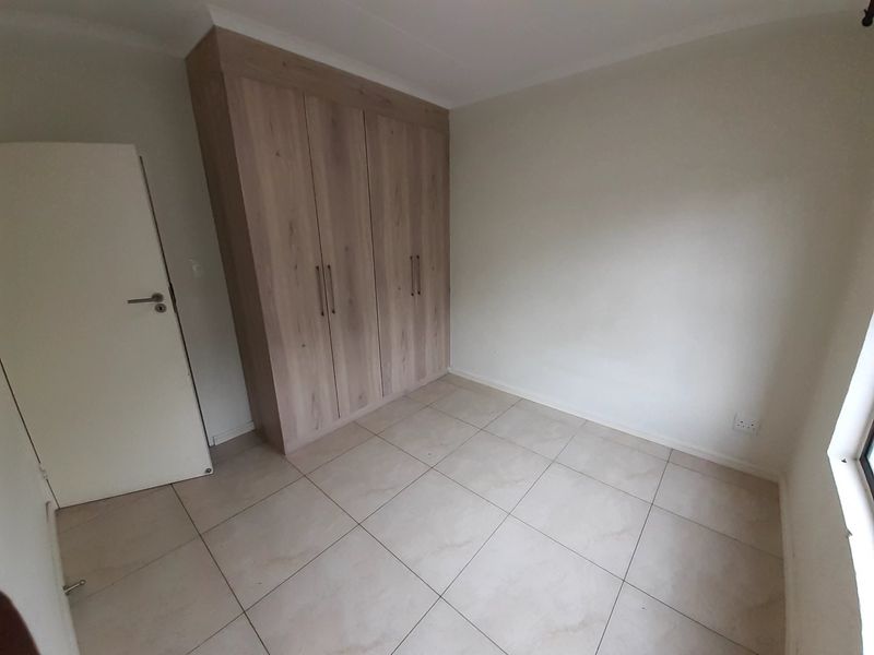 A clean, empty bedroom featuring neutral tiled flooring and modern wood-finish built-in cupboards, providing a versatile space ready for personalization.