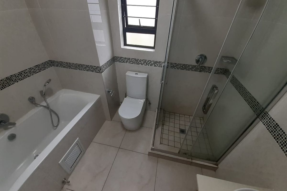 A clean, modern bathroom featuring a separate bathtub, glass-enclosed shower, and toilet with neutral wall and floor tiling.
