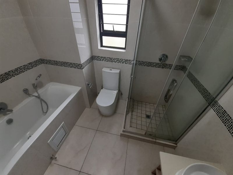 A clean, modern bathroom featuring a separate bathtub, glass-enclosed shower, and toilet with neutral wall and floor tiling.
