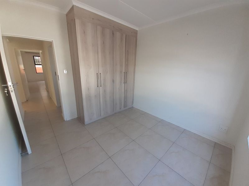 A bright, empty bedroom featuring neutral tiled flooring and modern built-in cupboards, offering a clean and versatile space.