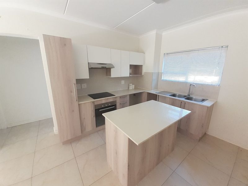 Modern kitchen featuring light wood-finish cabinetry, a central island, built-in oven and hob, and tiled flooring in a clean, open-plan layout.