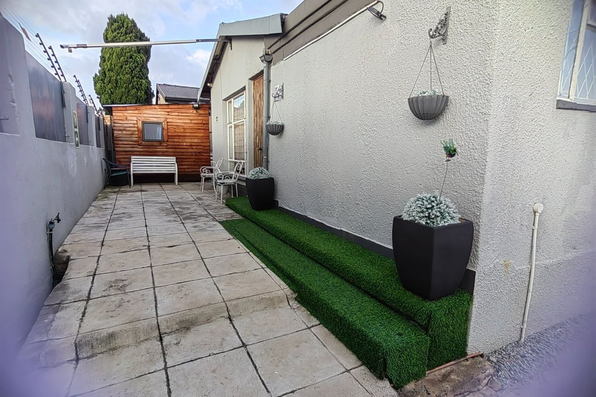 A paved rear courtyard area featuring artificial grass steps, a timber-clad outbuilding, and perimeter electric fencing.