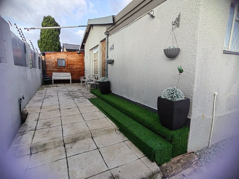 A paved rear courtyard area featuring artificial grass steps, a timber-clad outbuilding, and perimeter electric fencing.