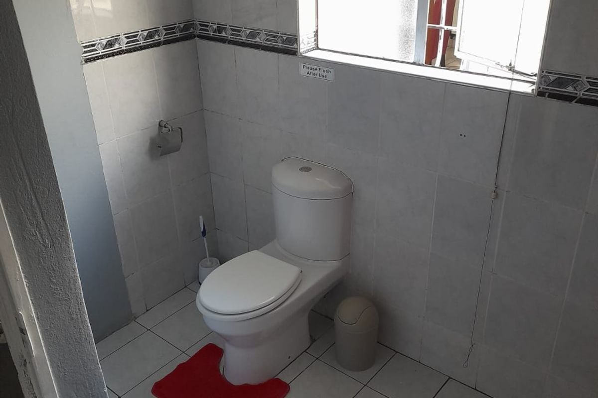 A functional bathroom featuring tiled walls and flooring, a standard toilet, and a window with a venetian blind.