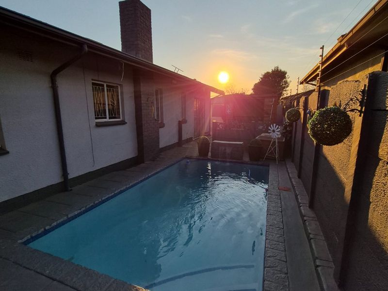 A well-maintained swimming pool area featuring a paved surround, brick chimney, and secure boundary wall, captured during sunset.