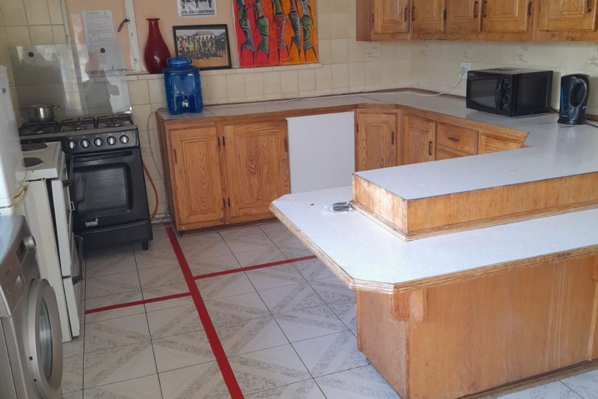 A functional kitchen featuring wooden cabinetry, laminate countertops, a gas stove, and tiled flooring, offering potential for a modern renovation.