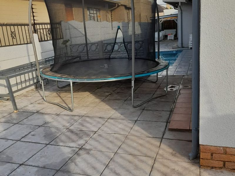 A paved outdoor patio area adjacent to the house, featuring a swimming pool and boundary wall enclosure.