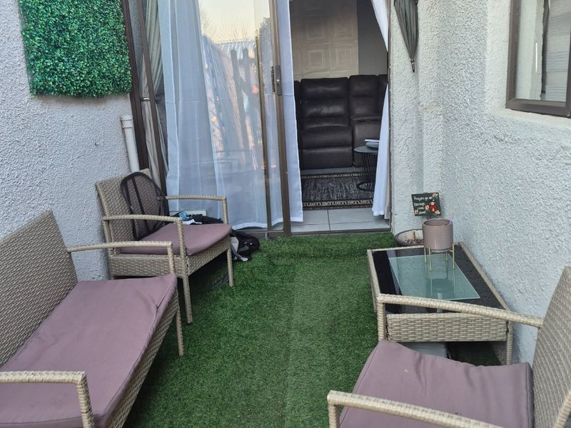 A compact outdoor patio area featuring artificial turf flooring and a sliding glass door providing access to the interior living space.