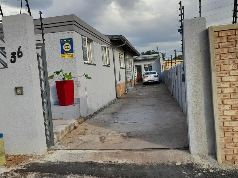 Front entrance view of the property featuring a concrete driveway, secure boundary walls with electric fencing, and a gated access point.
