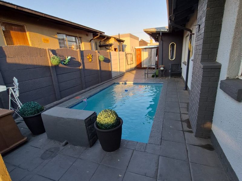 A compact outdoor pool area featuring a paved patio surround and enclosed by a precast concrete boundary wall.