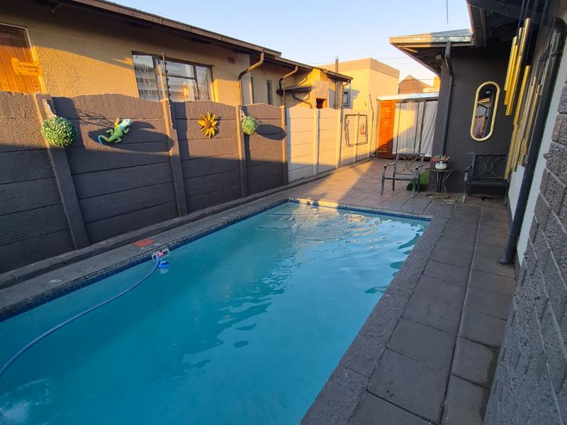 A narrow outdoor pool area featuring a rectangular swimming pool with paved surround and precast concrete boundary walls.