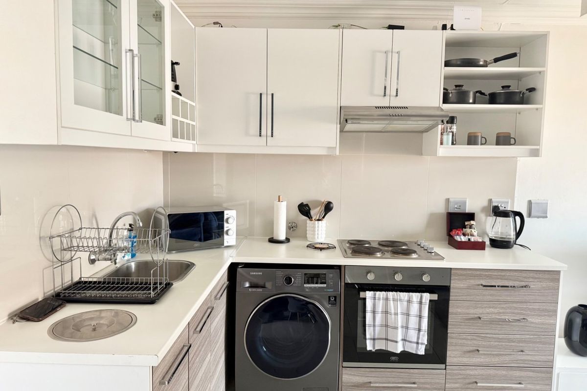A modern, well-maintained kitchen featuring white upper cabinetry, wood-grain lower cabinets, integrated appliances, and a clean tiled splashback.