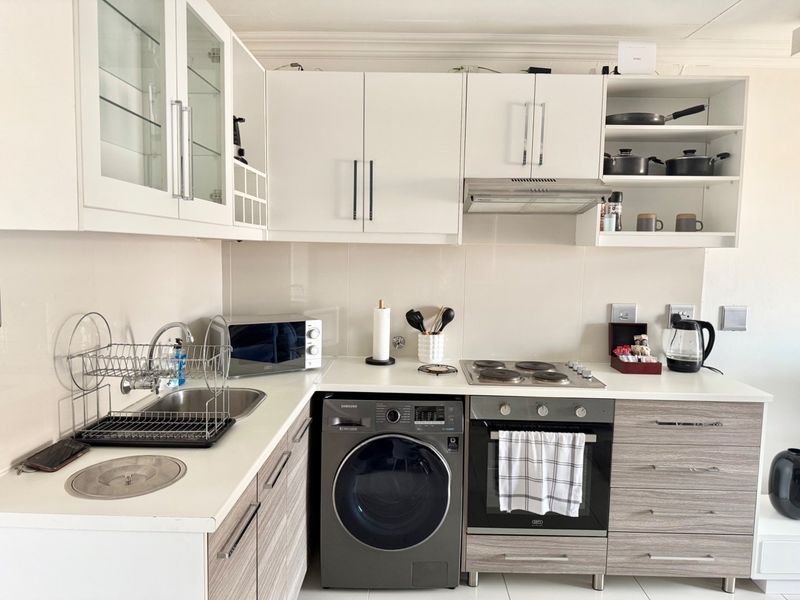 A modern, well-maintained kitchen featuring white upper cabinetry, wood-grain lower cabinets, integrated appliances, and a clean tiled splashback.